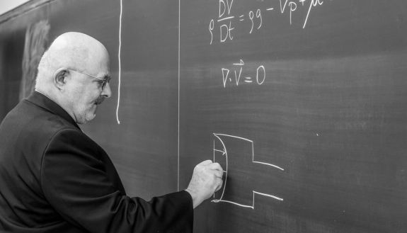 Old photo of a teacher at a chalkboard writing out formulas