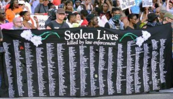 Protesters in Ferguson, Mo. holding up a Stolen Lives Project banner listing people killed by policemen. | Photo credit: Loavesofbread